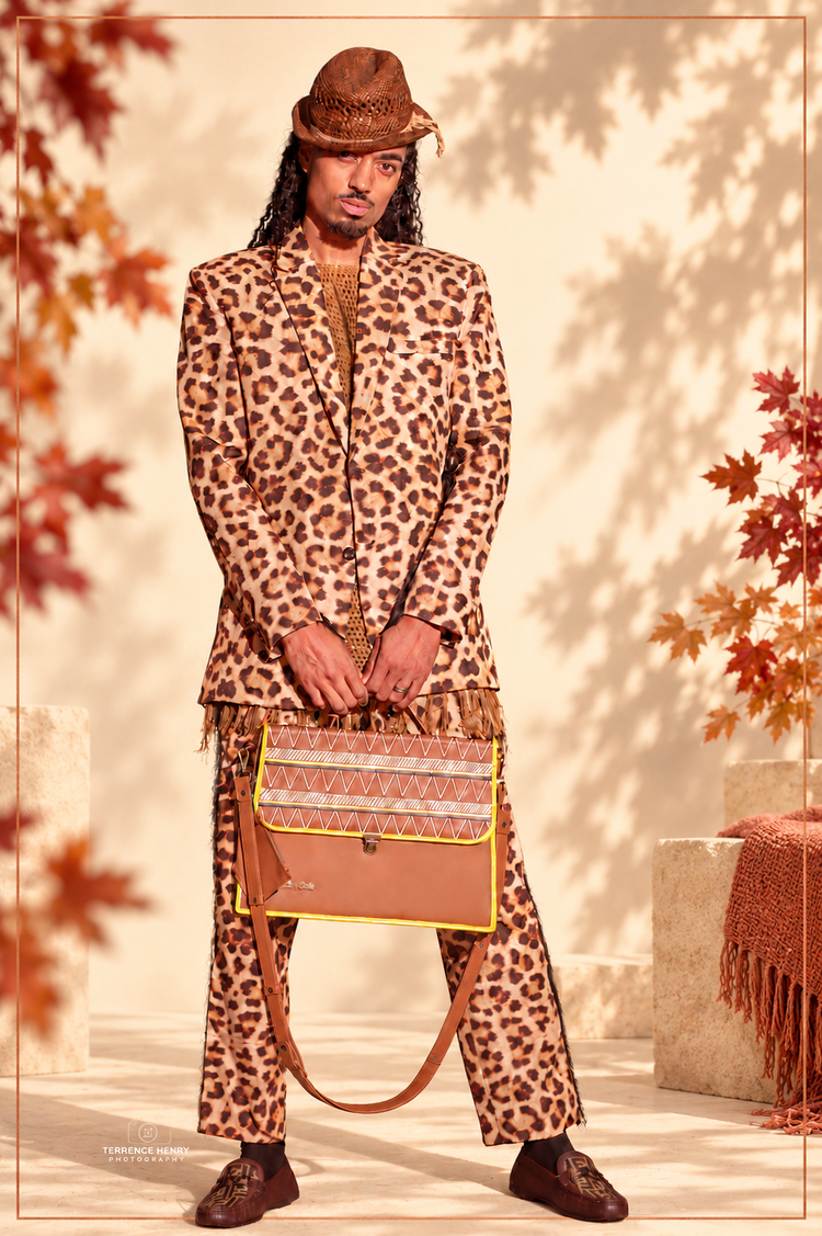 Man in a leopard-print suit holding the Earthsong unisex Brief Bag, framed by soft autumn leaf shadows and warm ivory and copper accents.