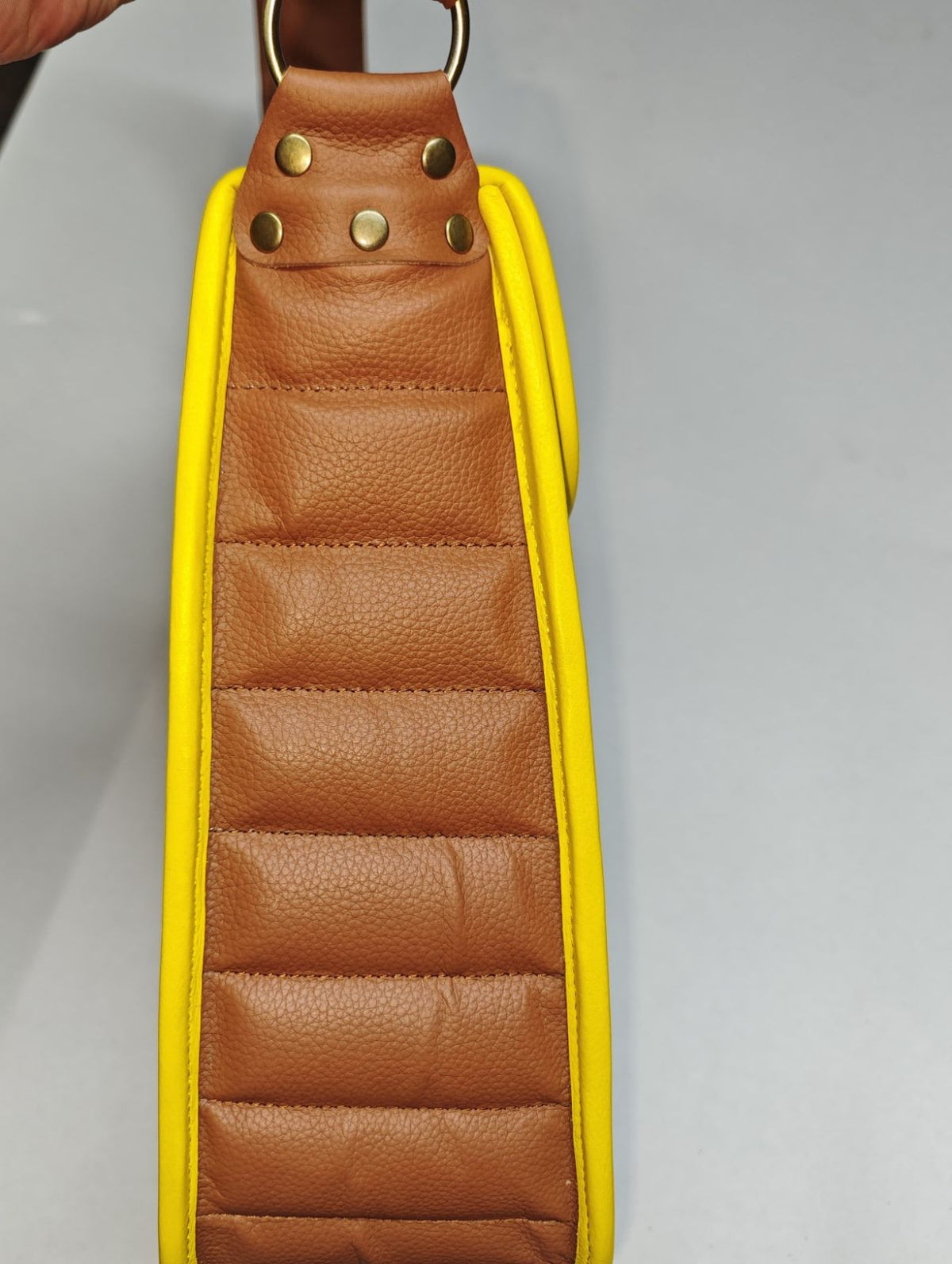 Side detail of the Earthsong Puff Bag showing puffed brown leather panels, yellow bound seams and gold-tone strap hardware.