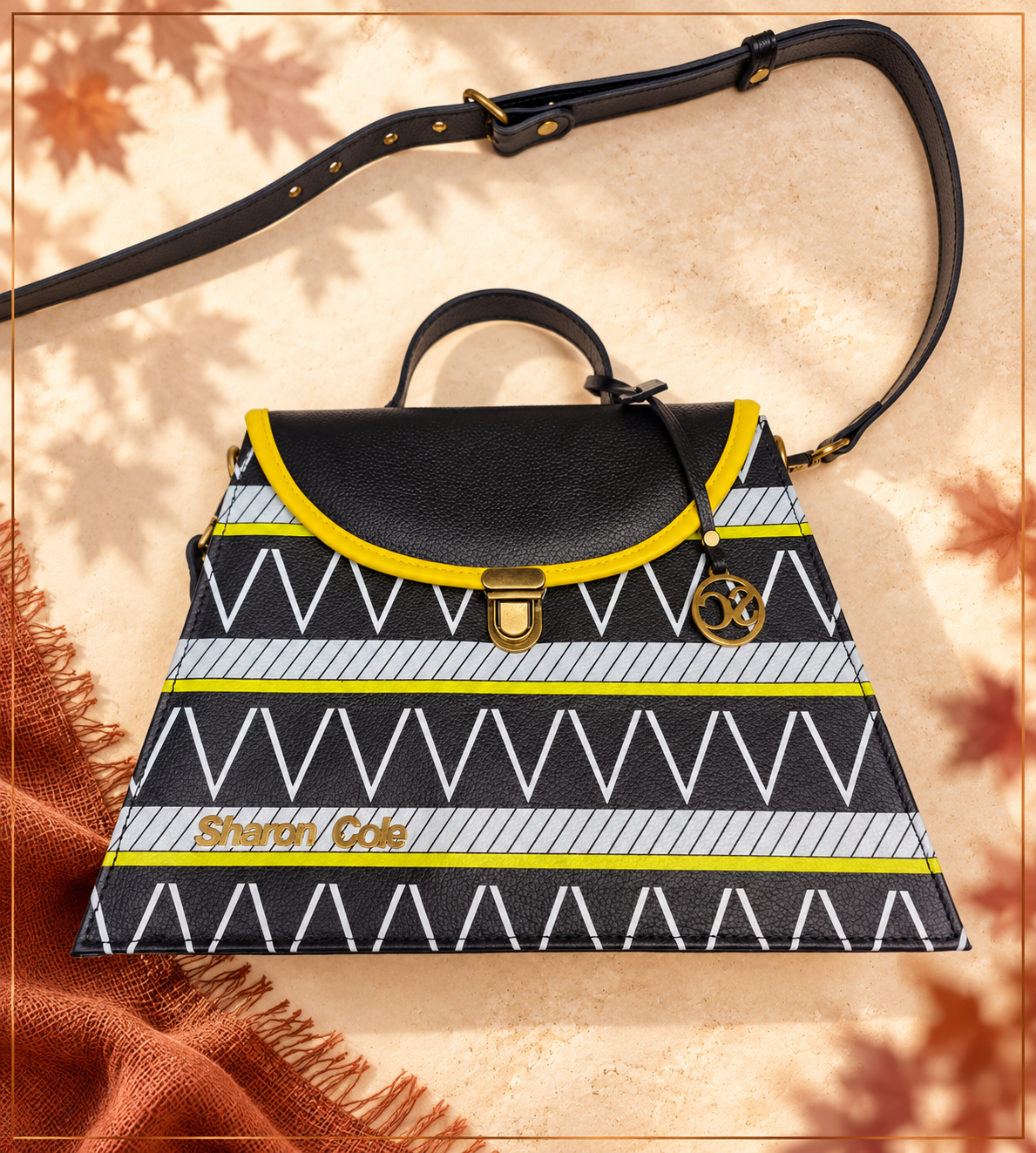Earthsong black leather handbag with yellow binding and tribal print on pale stone, with soft maple-leaf shadows and rust fringed linen.