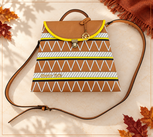 Earthsong brown leather handbag shown alone on pale ivory stone, with autumn leaf shadows, copper framing and rust fringed linen.